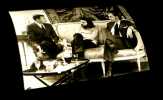[Photographie originale figurant Alain Robbe-Grillet, Jean-Louis Trintignant et Philippe Noiret au cours du tournage du film  Le Jeu avec le feu]. . ...