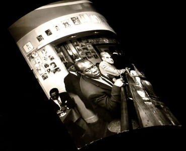 [Photographie originale figurant Louis Armstrong accoudé au comptoir d'un estaminet].