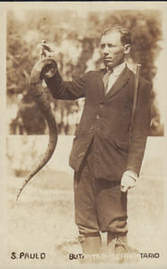 Carte postale photographique représentant un homme tenant un serpent à bout de bras.-