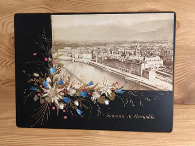 Photographie ancienne:  Souvenir de Grenoble. Vue Générale avec le massif de Belledonne. Photographie originale sur fond noir cartonné. 15 cm x 22 cm. décor de fleurs alpestres finement collées. edelweiss. ( environ 1900 )